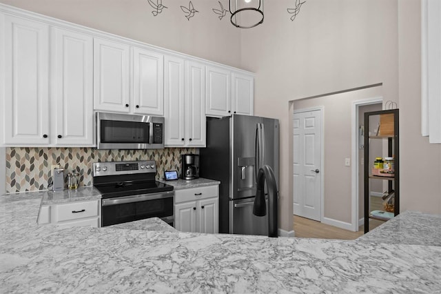 kitchen featuring appliances with stainless steel finishes, white cabinets, decorative backsplash, a high ceiling, and light stone countertops