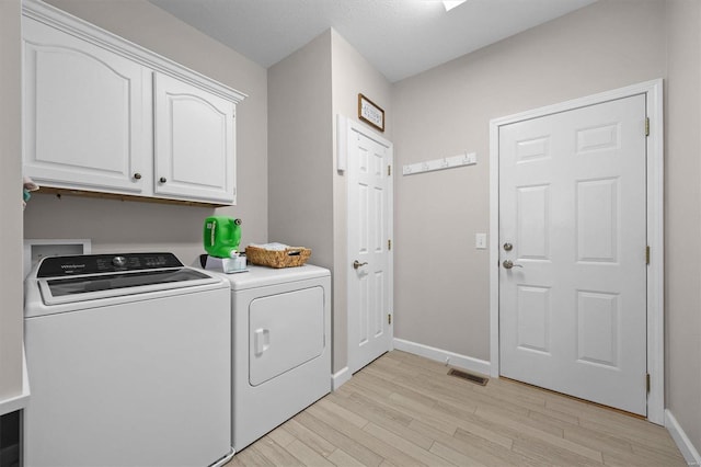 laundry room with cabinets, washing machine and dryer, and light hardwood / wood-style floors