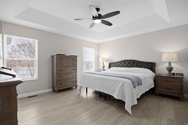 bedroom with ceiling fan, a tray ceiling, and light hardwood / wood-style floors