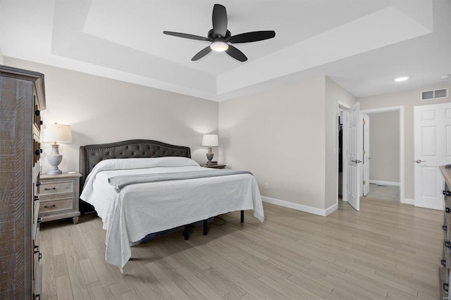 bedroom with light hardwood / wood-style flooring, ceiling fan, and a tray ceiling