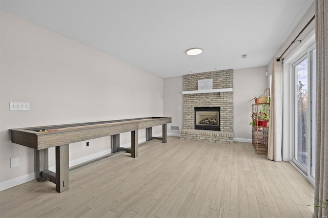 rec room with a brick fireplace and light wood-type flooring