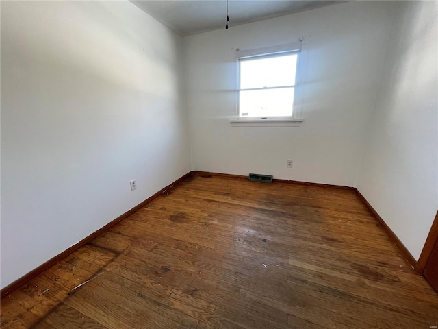 unfurnished room with dark wood-style flooring, visible vents, and baseboards