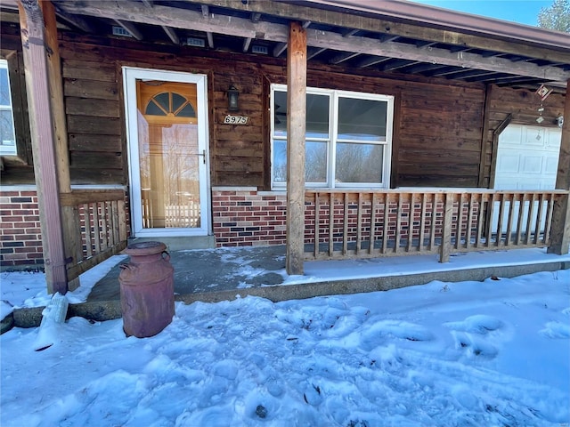 snow covered property entrance featuring a garage and brick siding