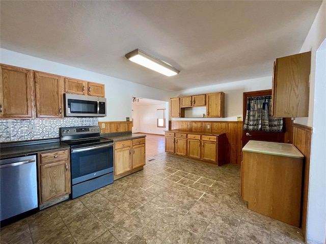 kitchen with dark countertops, tasteful backsplash, appliances with stainless steel finishes, and brown cabinets