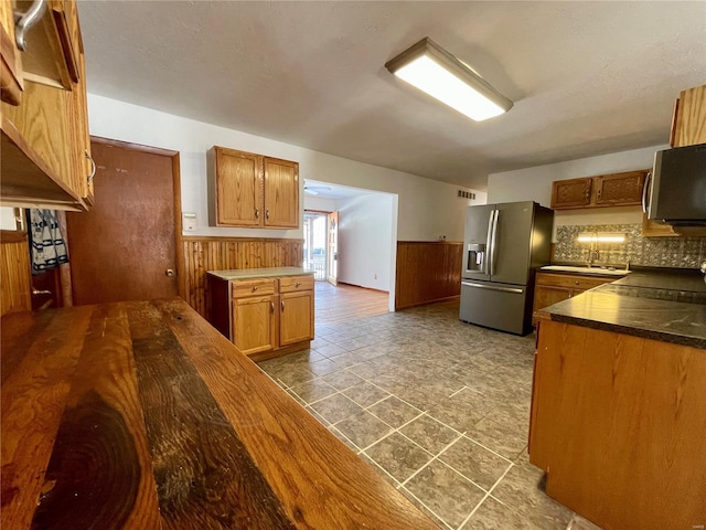 kitchen featuring a wainscoted wall, brown cabinets, dark countertops, appliances with stainless steel finishes, and wooden walls