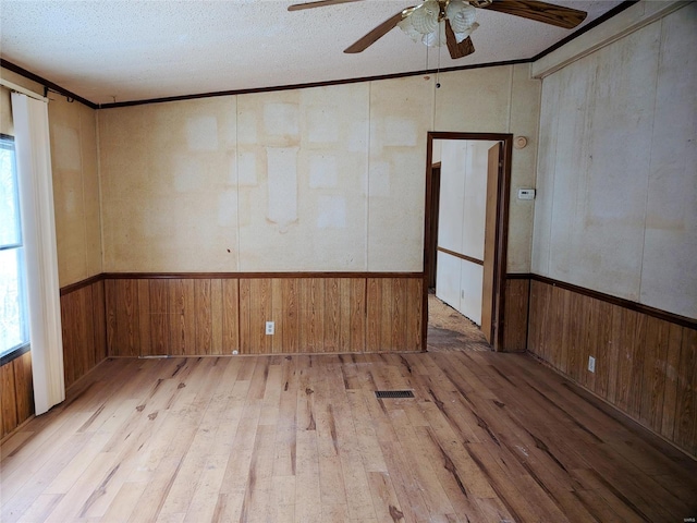 unfurnished room with crown molding, a textured ceiling, light wood-type flooring, wooden walls, and ceiling fan