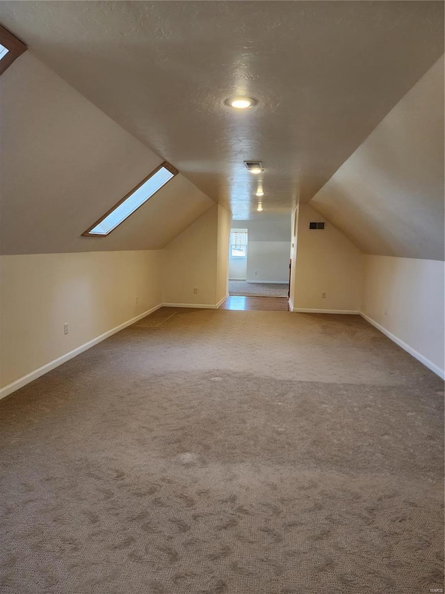 additional living space featuring lofted ceiling with skylight, a textured ceiling, and carpet flooring