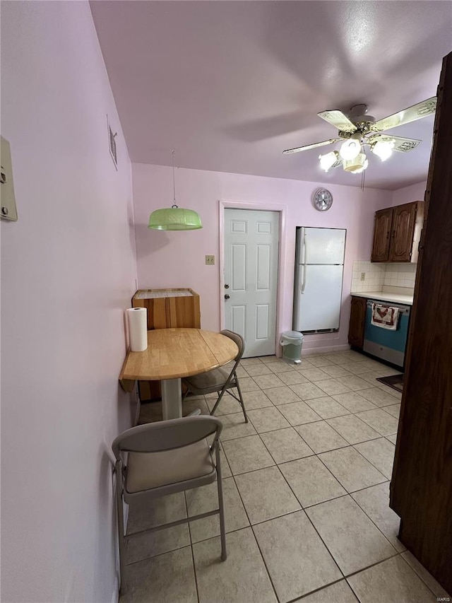 kitchen featuring dark brown cabinets, light tile patterned floors, dishwashing machine, white fridge, and decorative backsplash