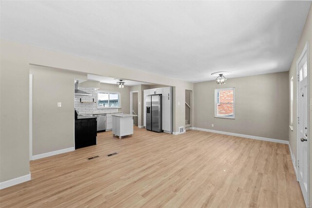 unfurnished living room featuring light wood finished floors, stairway, visible vents, and baseboards