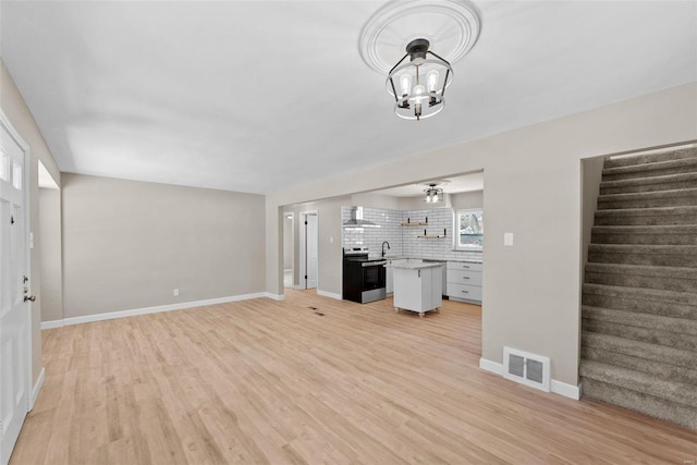 unfurnished living room featuring baseboards, stairway, visible vents, and light wood-style floors