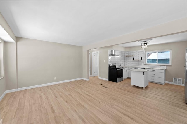 kitchen featuring wall chimney exhaust hood, open floor plan, a center island, stainless steel electric stove, and light countertops