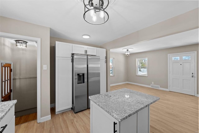 kitchen featuring stainless steel fridge, visible vents, white cabinetry, and light stone counters