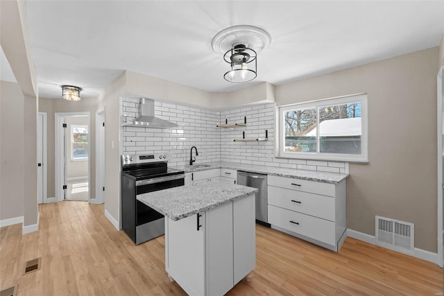 kitchen featuring a center island, open shelves, appliances with stainless steel finishes, white cabinets, and wall chimney range hood