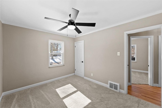 unfurnished bedroom featuring baseboards, visible vents, light colored carpet, ceiling fan, and ornamental molding