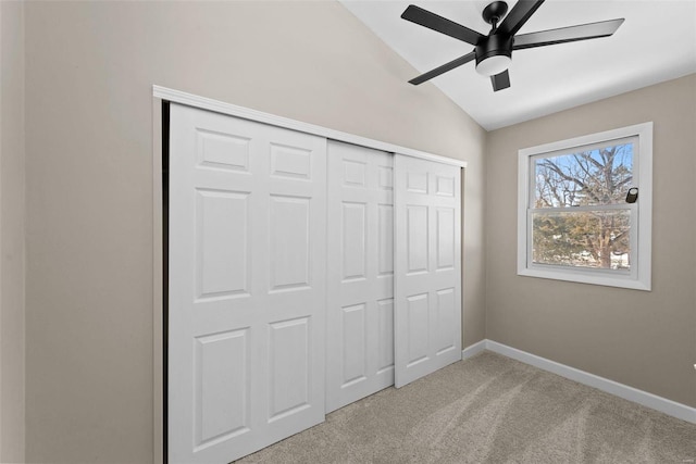 unfurnished bedroom featuring lofted ceiling, a closet, light colored carpet, a ceiling fan, and baseboards