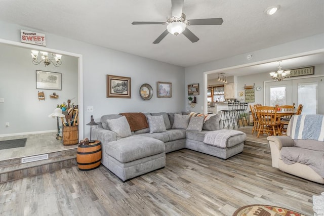 living room with hardwood / wood-style floors, ceiling fan with notable chandelier, and french doors