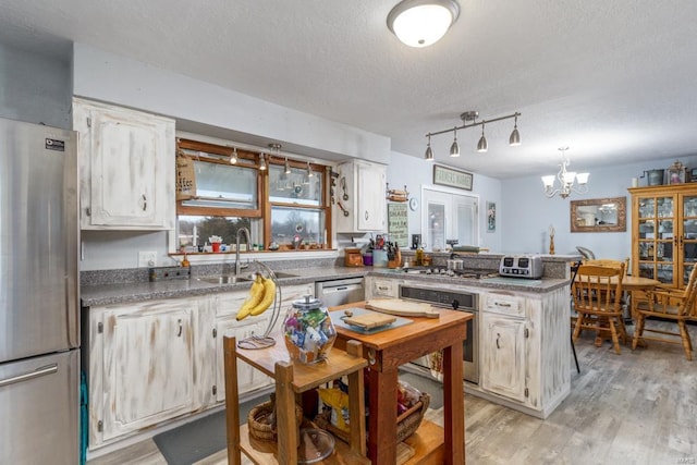 kitchen with sink, a textured ceiling, kitchen peninsula, stainless steel appliances, and light hardwood / wood-style floors