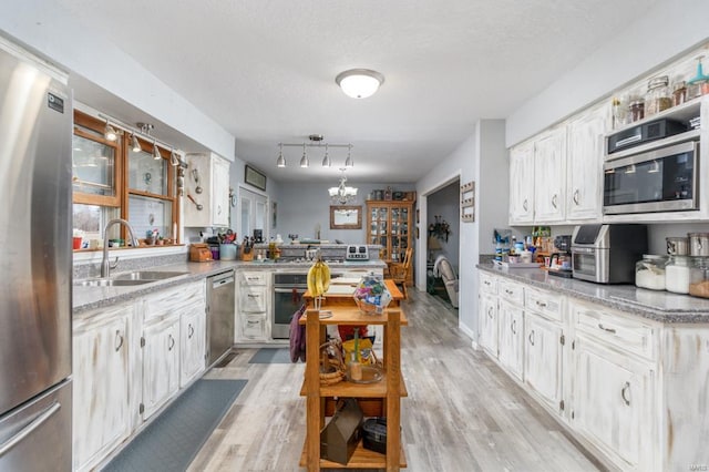 kitchen featuring sink, white cabinetry, an inviting chandelier, stainless steel appliances, and light hardwood / wood-style floors