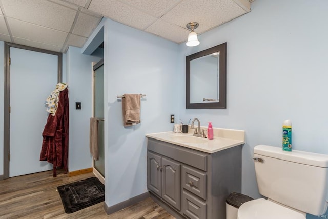 bathroom featuring hardwood / wood-style flooring, vanity, toilet, a shower with door, and a drop ceiling