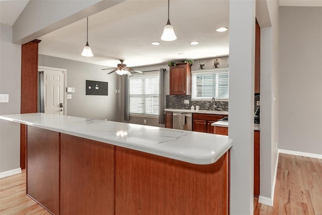 kitchen featuring decorative light fixtures, backsplash, stainless steel dishwasher, light stone counters, and light hardwood / wood-style flooring