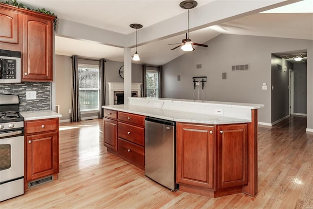 kitchen featuring stainless steel gas range, refrigerator, a center island, light wood-type flooring, and decorative backsplash