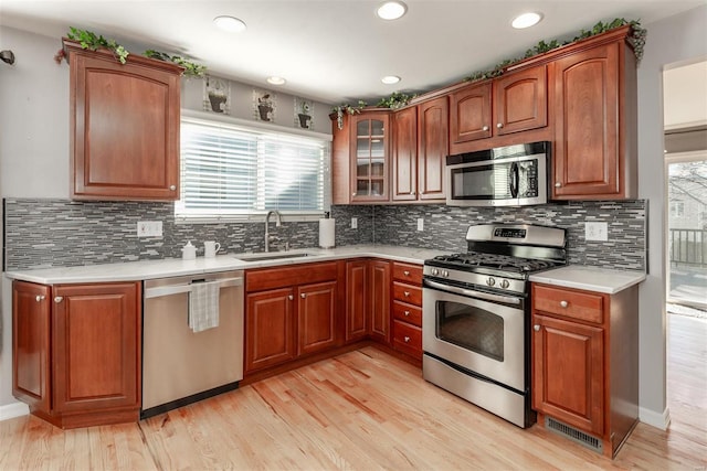 kitchen with tasteful backsplash, sink, light wood-type flooring, and appliances with stainless steel finishes