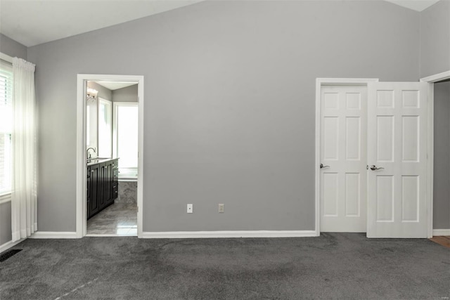 unfurnished bedroom with lofted ceiling, connected bathroom, sink, and dark colored carpet