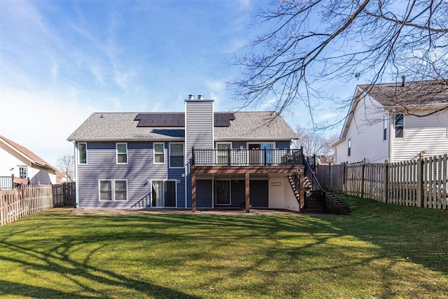 rear view of house with a patio area, a yard, a deck, and solar panels