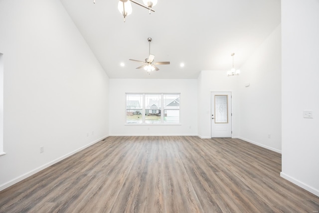 unfurnished living room with dark hardwood / wood-style flooring, ceiling fan with notable chandelier, and high vaulted ceiling