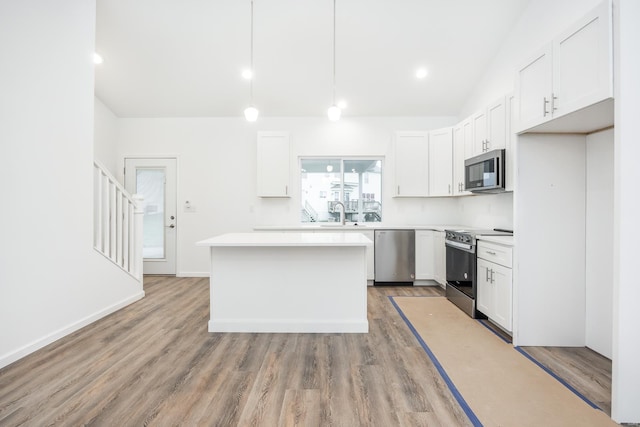 kitchen featuring a kitchen island, appliances with stainless steel finishes, white cabinets, and decorative light fixtures