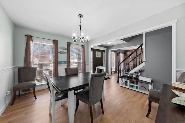 dining room featuring light wood-style floors, a wainscoted wall, an inviting chandelier, and stairs