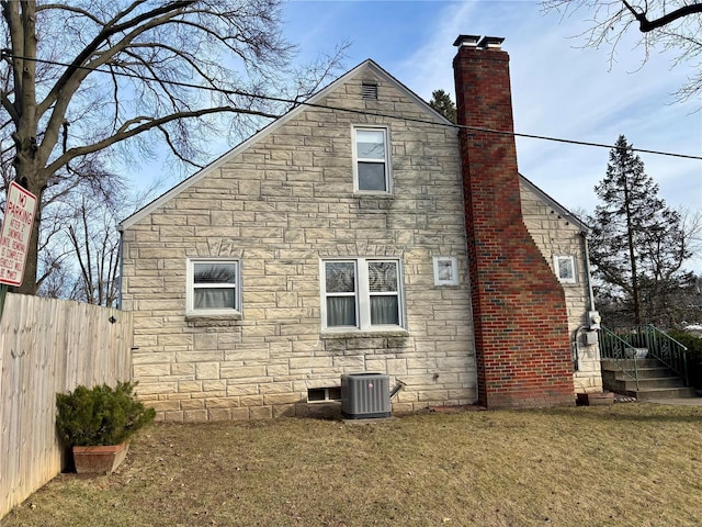 view of home's exterior featuring central AC unit, stone siding, a chimney, fence, and a yard