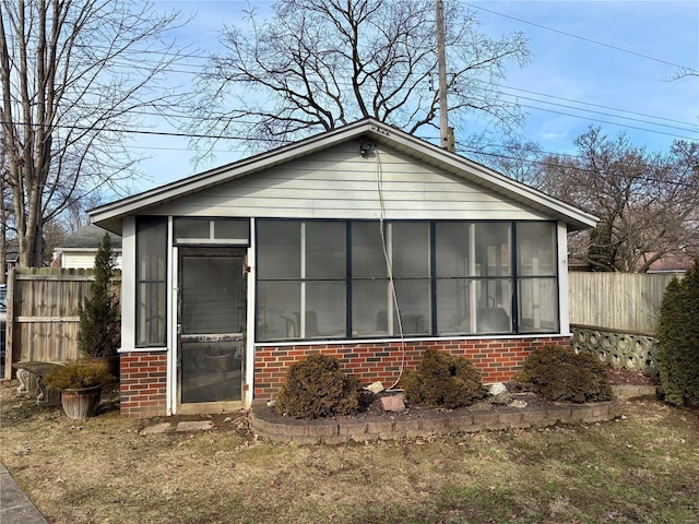 exterior space featuring brick siding, fence, and a sunroom