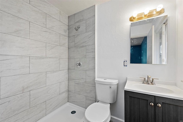 full bath featuring toilet, a tile shower, and vanity