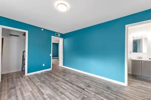 unfurnished bedroom with a closet, visible vents, ensuite bath, wood finished floors, and baseboards