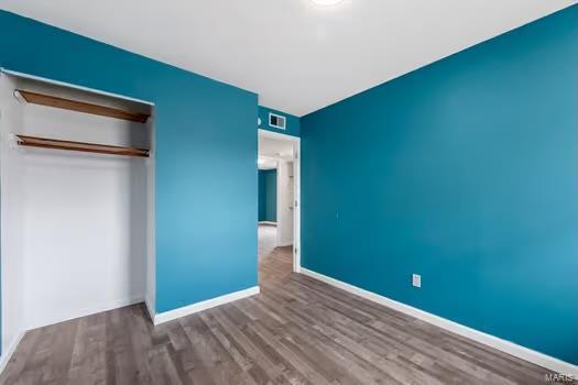 unfurnished bedroom featuring a closet, visible vents, baseboards, and wood finished floors