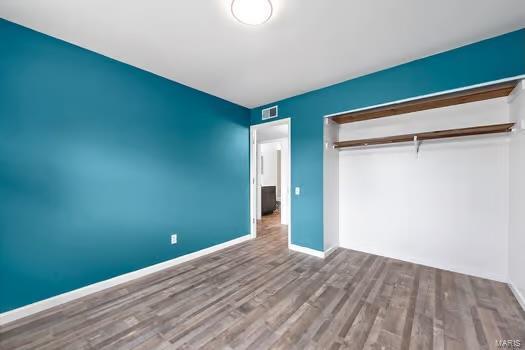 unfurnished bedroom with baseboards, a closet, visible vents, and wood finished floors