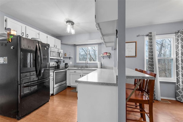 kitchen featuring white cabinetry, sink, a breakfast bar area, light hardwood / wood-style floors, and stainless steel appliances