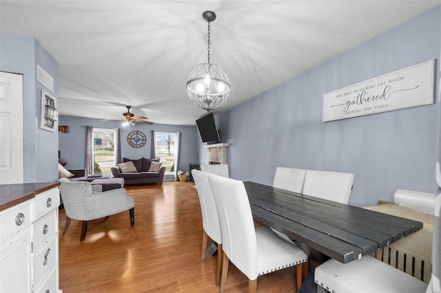 dining space with ceiling fan with notable chandelier and light hardwood / wood-style flooring