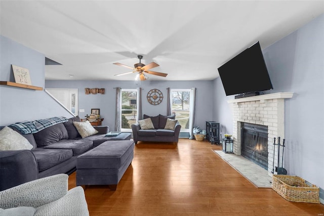 living room featuring wood-type flooring, a brick fireplace, and ceiling fan