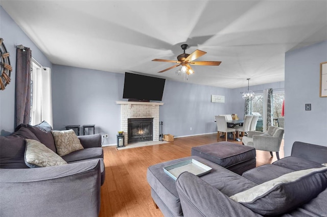 living room with a brick fireplace, ceiling fan with notable chandelier, and light hardwood / wood-style flooring