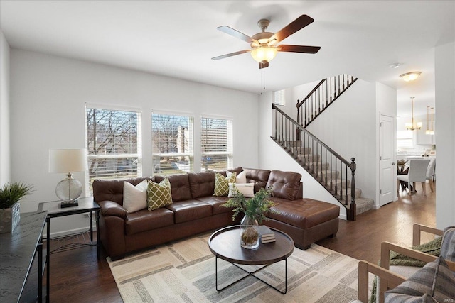 living area featuring stairway, light wood-style flooring, and ceiling fan with notable chandelier