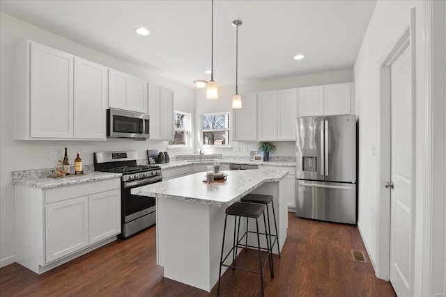 kitchen with visible vents, a kitchen island, stainless steel appliances, white cabinets, and a kitchen breakfast bar