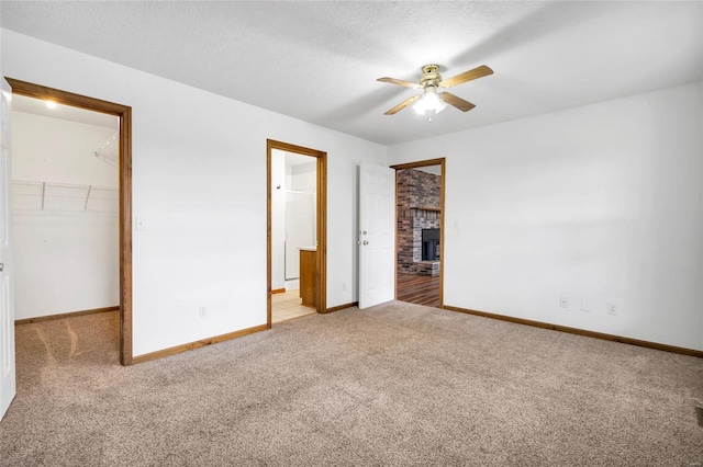 unfurnished bedroom with a spacious closet, a brick fireplace, a textured ceiling, a closet, and light colored carpet