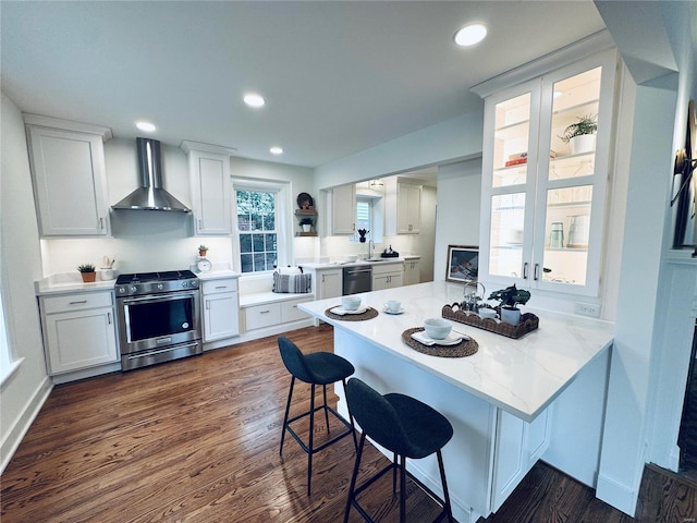 kitchen with stainless steel stove, a breakfast bar, white cabinets, kitchen peninsula, and wall chimney exhaust hood