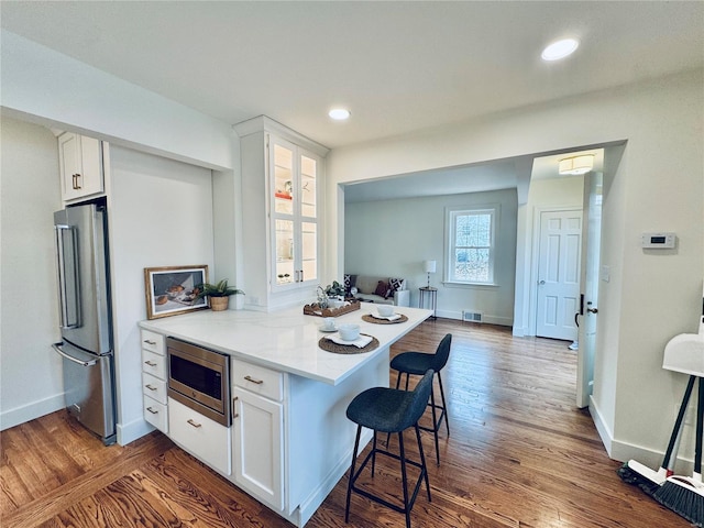 kitchen featuring a kitchen bar, white cabinetry, dark hardwood / wood-style flooring, kitchen peninsula, and stainless steel appliances