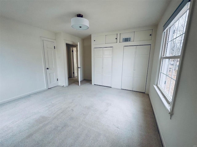 unfurnished bedroom featuring multiple windows, light carpet, and two closets