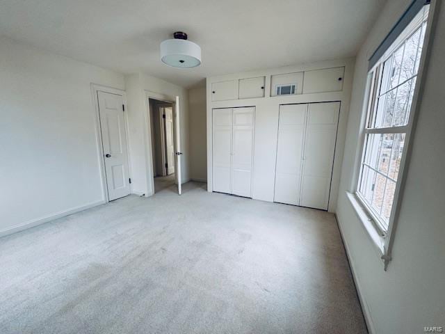 unfurnished bedroom with light carpet, two closets, and multiple windows