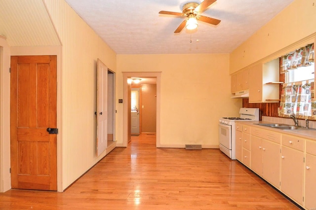 kitchen featuring sink, ceiling fan, white cabinetry, white gas stove, and light wood-type flooring