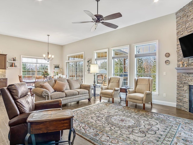 living room with hardwood / wood-style flooring, a stone fireplace, and ceiling fan with notable chandelier